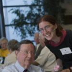 Member of the Class of 1951 holding a pink rose with another person at a forum in 2006