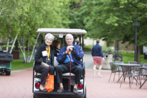 Two members of the Class of 1966 riding in the back of a golf cart at Reunion 2016