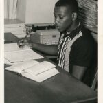 Photo of Jesse Jones, Class of 1966, sitting at a desk writing in a notebook