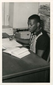 Photo of Jesse Jones, Class of 1966, sitting at a desk writing in a notebook