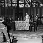 The Reverend Al Currier at the center of the Chapel in Fall 1968, with musicians behind him, and others in the pews in front of him