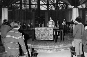 The Reverend Al Currier at the center of the Chapel in Fall 1968, with musicians behind him, and others in the pews in front of him