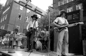 Musicians on stage on front of Old Main; Labor Day Sunday, 1969, found most everyone on campus parked lazily in front of Old Main, enjoying the first rock concert of the school year. Among the performers were MUSHROOM, featuring (L to R) Tommy Wiesner, Rob Dimit, John Katsantonis