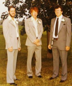 Photo of Jim Phillips, Don Hill, and Joel Stegner standing, all three in suits with flowers in their lapels