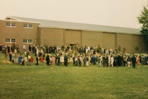 Macalester graduates and family and friends on the lawn in front of the gym