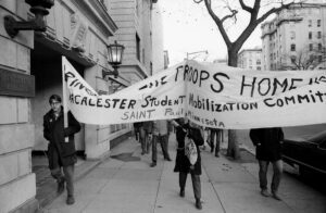 Students walking with a huge banner at the March on Washington in November 1969; the part of the banner that is visible reads, "Bring the Troops Home; Macalester Student Mobilization Committee; Saint Paul, Minnesota"