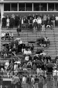 Spectators, many holding umbrellas, in the bleacher seats at MIAC track meet, Spring 1969