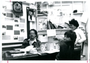 Candid office photo including Alan Maranville, Class of 1971, seated at a desk