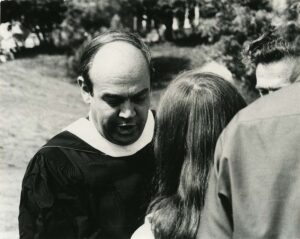 A person in a commencement robe faces the camera but is looking down, at Commencement 1976