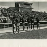 Six students in cheer uniforms on the stadium field