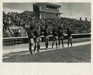Six students in cheer uniforms on the stadium field