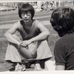 black and white photo of student sitting on a skateboard talking with friends