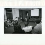 Mayor Cisneros standing at the front of the Fine Arts Lounge speaking to groups of students seated around him in October 1985