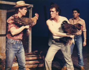 Three performers on stage in Roosters in 1988; two of the performers are holdig roosters