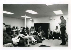 Vernon Bellecourt. standing at the front of a room, speaking to students in April 1990
