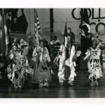 Four people holding flags in traditional dress at the 1989 pow wow at Mac