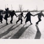 Six students holding hands, walking in a chain, across the ice skting rink on campus, 1/18/1989