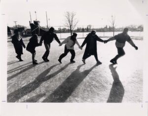 Six students holding hands, walking in a chain, across the ice skting rink on campus, 1/18/1989