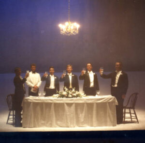Six performers standing with raised glasses at a table on stage in Terra Nova 1987