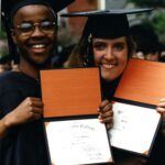 Two students in caps and gowns, showing off their diplomas, at Commencement 1996