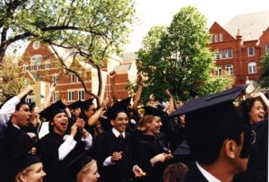 Group of smiling graduates in caps and gowns in front of Old Main at Commencement 1996