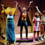 Six character from the 2008 production of the Colored Museum holding their arms in the air