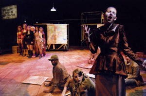 An image from the 2008 production of the Threepenny Opera. Half the characters are in a group, far away from the camera looking at the other half, which are next to the camera.