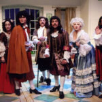 An image from the 2009 production of the Tartuffe. Seven characters are looking straight forward with various looks of distress.
