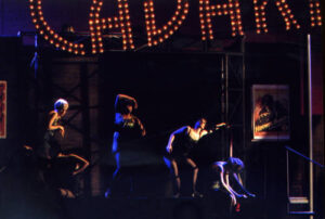 An image from the 2010 production of Cabaret. Five characters in dark lighting, dancing.