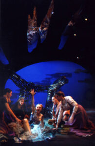 An image from the production of Ophelias. Four characters gathered around an other character who is on the floor screaming and raising an arm in the air