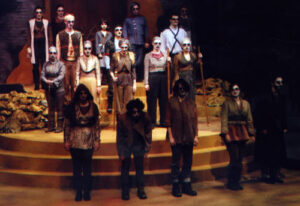 An image from the 2011 production of Antigone. The cast is standing in rows looking at the audience.