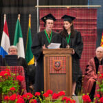 Two Mac students at a pedestal giving a speech during commencement.