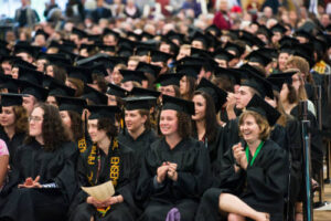 Students sitting in the field house in their caps and gowns during commencement